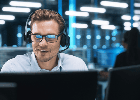 Male customer service representative with headset smiling while working at computer in modern office